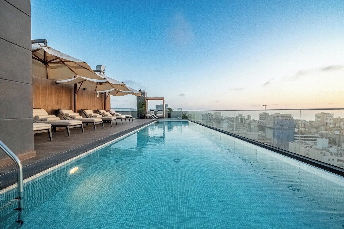 A rooftop infinity pool with lounge chairs and umbrellas, offering a city view.