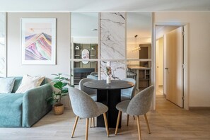 Ein modernes Wohnzimmer mit einer Couch, einem Esstisch mit Stühlen, einer Topfpflanze und einem großen abstrakten Gemälde an der Wand.