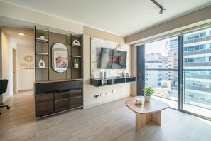 Ein modernes Wohnzimmer mit großem Fernseher, Couchtisch und Blick auf die Stadt.