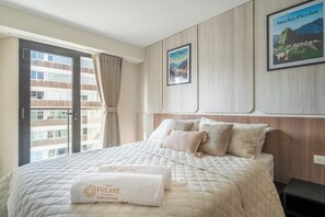 Ein Hotelzimmer mit einem großen Bett, einem Vorhangfenster, einem gerahmten Bild an der Wand und einem Handtuch mit dem Hotelnamen.