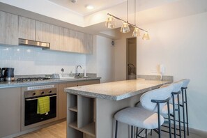 Una cocina moderna con una isla central, taburetes de bar, horno empotrado y extractor de acero inoxidable.