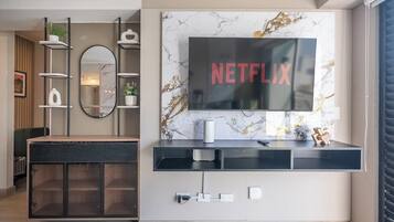 Un soggiorno moderno con TV a parete che mostra 'NETFLIX', un mobile contenitore in legno con ante in vetro, un tavolino consolle nero e una parete con decoro marmorizzato.