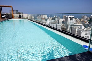 Une piscine sur le toit offrant une vue sur la ville, avec une eau cristalline et une balustrade en verre.