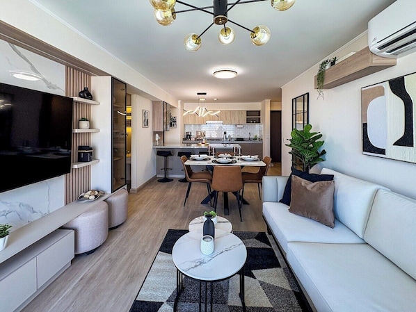 Ein modernes Wohnzimmer mit einem Flachbildfernseher, einer Couch, einem Couchtisch und einem Essbereich mit Tisch und Stühlen.