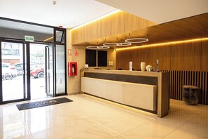 Un hall d’hôtel avec un comptoir d’accueil en bois, un extincteur et un panneau indiquant « SORTIE ».