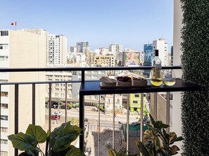 En balkon med udsigt over byen, et bord med ting på, og krukkeplanter.