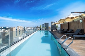 Ein Infinity-Pool auf dem Dach mit Blick auf die Stadt, Liegestühle und Sonnenschirme.