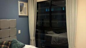 Et hotelværelse med en seng, en sengegavl, et vindue med gardiner og et billede hængt på væggen.