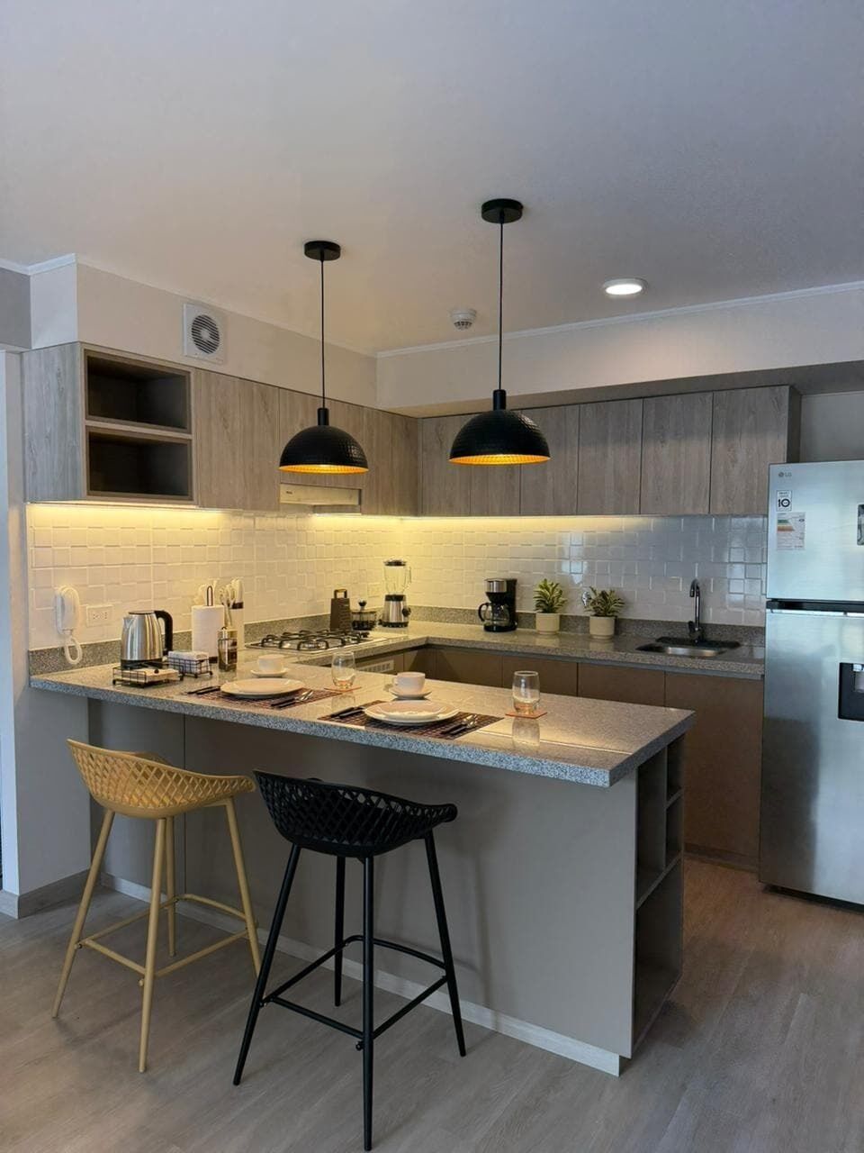 A modern kitchen with a central island, two bar stools, pendant lighting, and a built-in refrigerator.