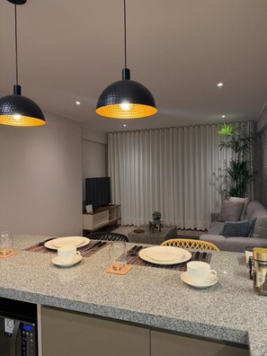 A modern kitchen with granite countertops, a dining area with a table set for two, and a living room with a sofa and curtains. - Modern apartment | Larco Av. | Miraflores (Miraflores)