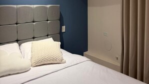Et hotelværelse med seng, sengegavl, vægmonteret skab og et vindue med gardiner.
