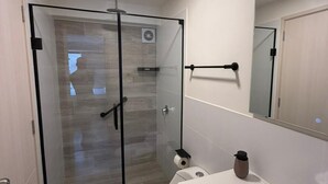 Et moderne badeværelse med bruseniche i glas, toilet, vask og spejl.