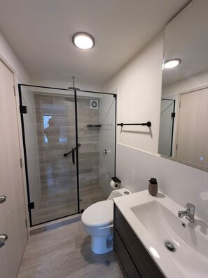 Ein modernes Badezimmer mit Duschkabine aus Glas, Toilette, Waschbecken und Spiegel.