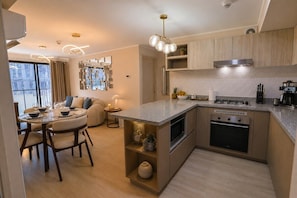 A modern kitchen with a central island, built-in oven, and a dining area with a round table and chairs. - Miraflores Boutique Escape | Pool · Rooftop · Gym (Miraflores)