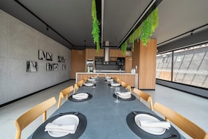 A modern dining area with a long table set for a meal, wooden chairs, and hanging greenery. - Miraflores Boutique Escape | Pool · Rooftop · Gym (Miraflores)
