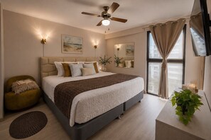 A bedroom with a bed, a ceiling fan, wall-mounted lights, a window with curtains, a bedside table with a plant, and a TV. - Miraflores Boutique Escape | Pool · Rooftop · Gym (Miraflores)