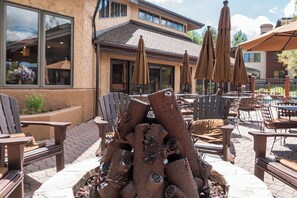 An outdoor seating area with wooden chairs and tables, a decorative metal sculpture, and umbrellas. - TL2303 | Top Floor | Perfect Steamboat Getaway | A/C | 10 Hot Tubs (Steamboat Springs)