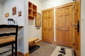Un pasillo con puertas de madera, un banco, un estante pequeño y una alfombra con estampados de animales.