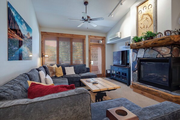 A living room with a sectional sofa, a wooden coffee table, a fireplace, and a television. - TL2304 | Beautifully Appointed | Vaulted Ceilings | A/C | 10 Hot Tubs (Steamboat Springs)