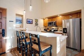 A modern kitchen with a central island, wooden cabinets, stainless steel appliances, and a bar stool seating arrangement. - TL2305 | Vaulted Ceiling | A/C | 10 Hot Tubs | 4 Pools | Close to Mtn (Steamboat Springs)