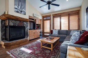 A living room with a stone fireplace, wooden cabinets, a grey sofa, and a ceiling fan. - TL2305 | Vaulted Ceiling | A/C | 10 Hot Tubs | 4 Pools | Close to Mtn (Steamboat Springs)