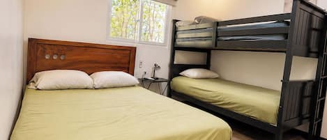 Habitación con una cama individual y una litera, piso de madera, una lámpara en el techo y una ventana con persianas.