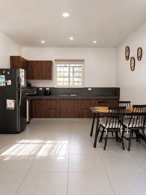 Eine moderne Küche mit dunklen Holzausziehtüren, einem schwarzen Kühlschrank, einem eingebauten Backofen und einem Essbereich mit rundem Tisch und Stühlen.
