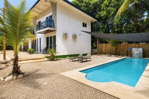 Ein modernes, zweistöckiges Haus mit Swimmingpool, Sitzgelegenheiten im Freien und einem Bambuszaun.