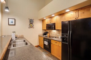 A kitchen with wooden cabinets, a black refrigerator, a microwave, and a stainless steel sink. - TL2310 | Spacious Top Floor Residence | A/C | Great Amenities (Steamboat Springs)