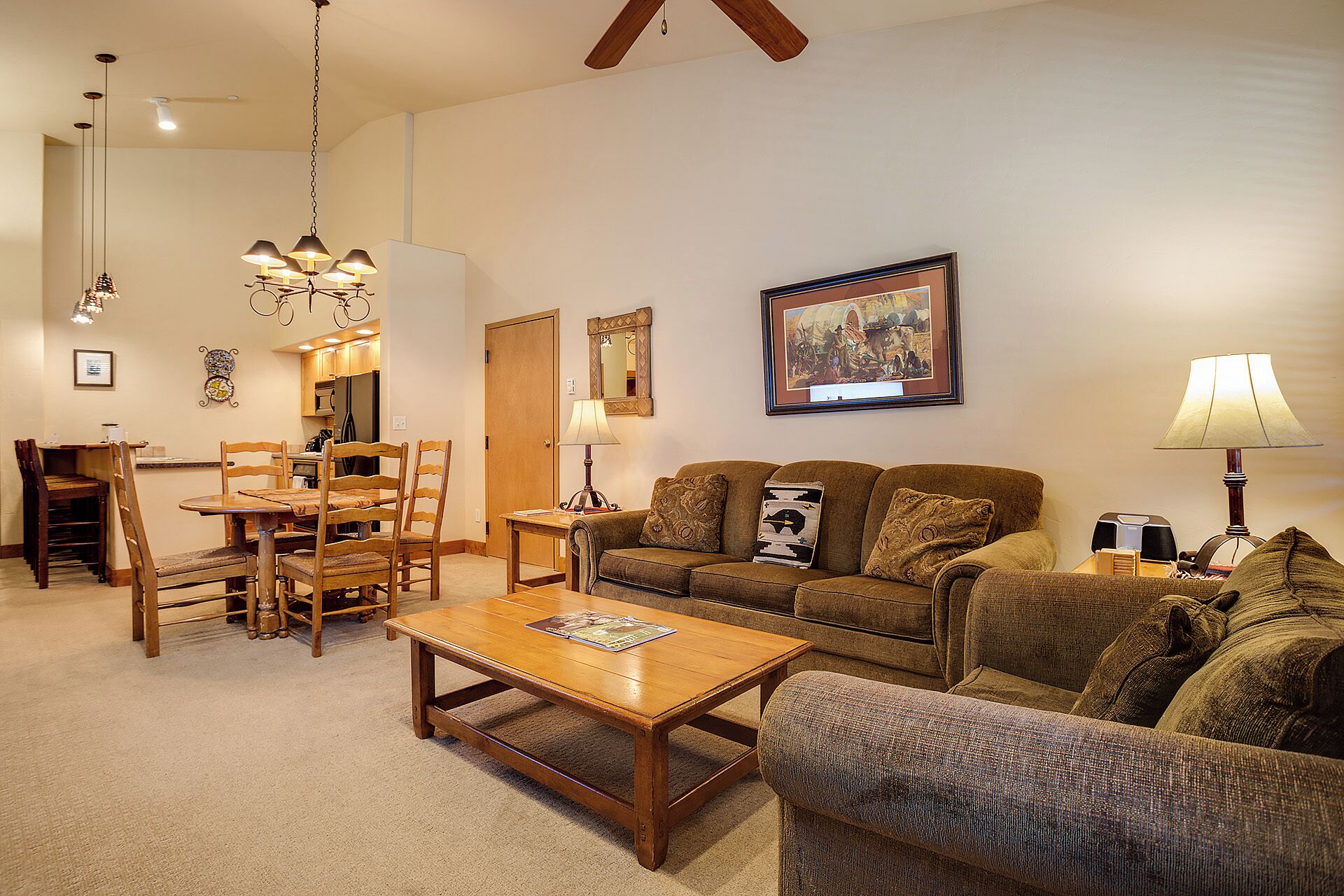 A living room with a wooden coffee table, two sofas, a dining table with chairs, and a kitchen area in the background.