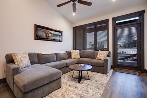 A living room with a sectional sofa, a coffee table, a painting on the wall, and large windows with blinds. - TL2311 | Great Views | Beautiful Top Floor with Vaulted Ceiling | Winter Shuttle (Steamboat Springs)
