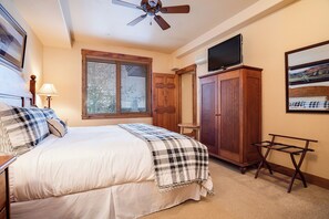 Ein Schlafzimmer mit einem Bett, einem Deckenventilator, einem Fenster mit Jalousien, einem Fernseher auf einem Schrank und einem gerahmten Bild an der Wand.