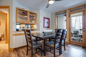 A dining area with a wooden table and chairs, a kitchen with wooden cabinets, and a large window with a view of trees. - TR1104 | Updated Corner Unit | Winter Shuttle | 10 Hot Tubs | Close to Skiing (Steamboat Springs)