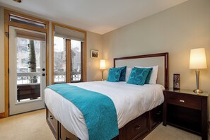 A bedroom with a large bed, two bedside lamps, a wooden nightstand, and a view through a glass door. - TR1104 | Updated Corner Unit | Winter Shuttle | 10 Hot Tubs | Close to Skiing (Steamboat Springs)