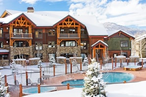 A multi-story lodge with a pool area, surrounded by snow-covered trees and mountains. - TR1104 | Updated Corner Unit | Winter Shuttle | 10 Hot Tubs | Close to Skiing (Steamboat Springs)