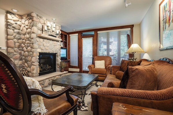 Una sala de estar acogedora con chimenea de piedra, muebles de cuero y televisor.