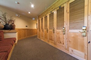 Un couloir avec des casiers en bois, un sol recouvert de moquette et un pot de fleurs placé sur le côté gauche.