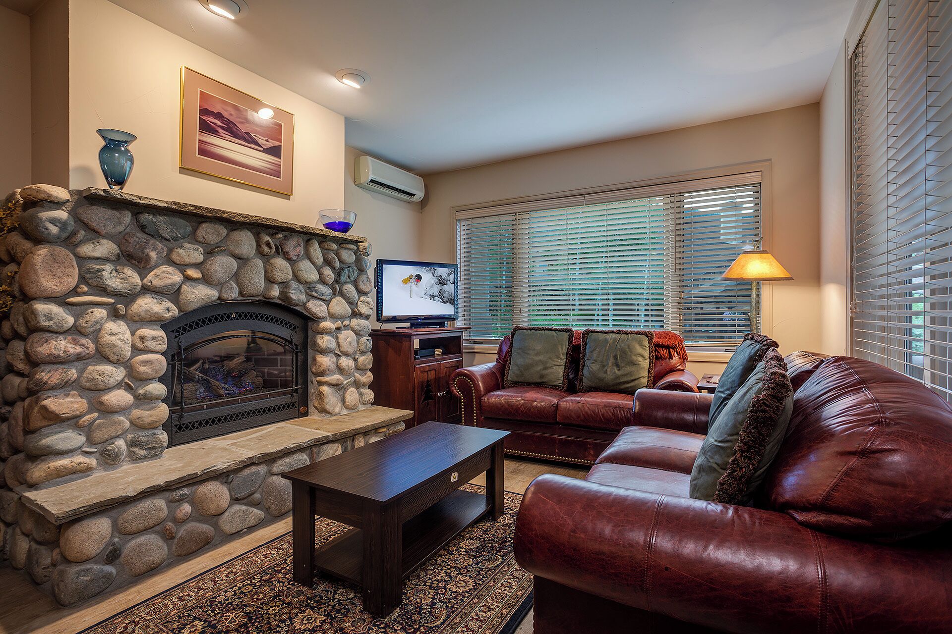 A living room with a stone fireplace, leather sofa, and a television.