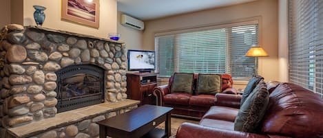 Una sala de estar con chimenea de piedra, sofá de cuero y televisor.