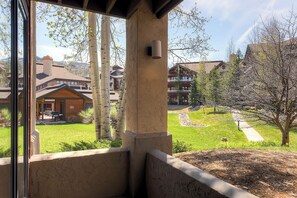 Blick von einem Balkon mit Steinmauer auf eine gepflegte Rasenfläche und ein Gebäude mit Holzfassade.