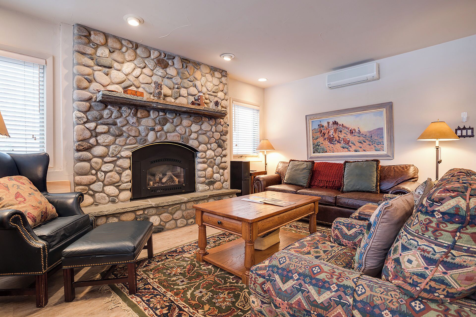 Ein Wohnzimmer mit Kamin aus Stein, Ledersofas, einem gemusterten Teppich und einem Gemälde an der Wand.