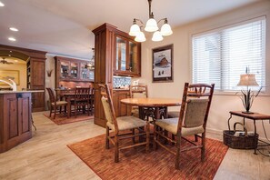 A dining area with a wooden table and chairs, a kitchen with wooden cabinets, and a window with blinds. - TR1111 | Perfect for families or group of couples | A/C | 10 Hot Tubs (Steamboat Springs)