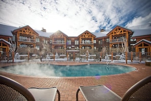 A poolside area with a hot tub, lounge chairs, and a building with multiple balconies. - TR1201 | Beautiful Home | Close to Skiing | A/C | 10 Hot Tubs (Steamboat Springs)