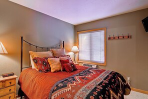 A bedroom with a bed, bedside table, lamp, window with blinds, and a wall-mounted coat rack. - TR1202 | Beautiful Décor | Close to Skiing | A/C | 10 Hot Tubs (Steamboat Springs)