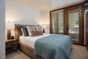A bedroom with a bed, bedside lamps, a nightstand, a window with blinds, and a door. - TR1203 | Close to Base Area | 10 Hot Tubs | Winter Shuttle | 4 Pools (Steamboat Springs)