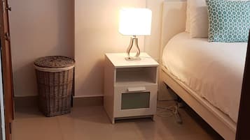 A bedroom with a bed, a nightstand with a lamp, a wicker basket, and a painting on the wall.