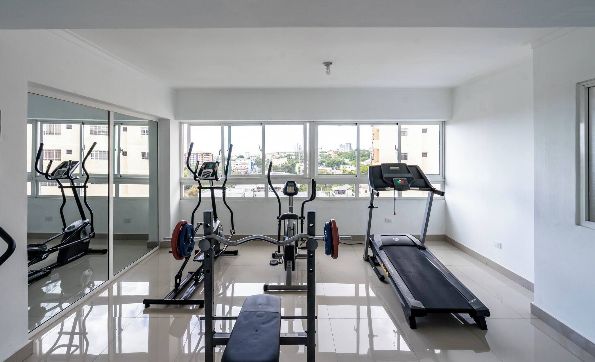 A gym with various exercise equipment, large windows, and a clean, tiled floor.