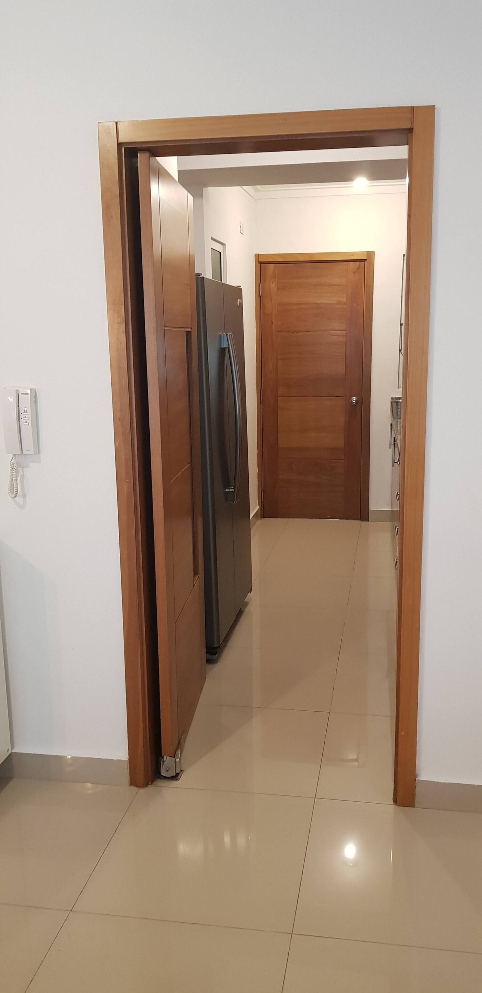 A hallway with a refrigerator and a wooden door at the end.