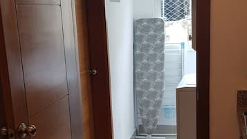 A hallway with a wooden door, a tiled floor, and a view into a room with a bed and a window.