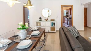 A modern living room with a dining area, a sofa, and a kitchen visible through an open door. - 2br Kingbed Kids Play Area No Surgery (Santo Domingo)